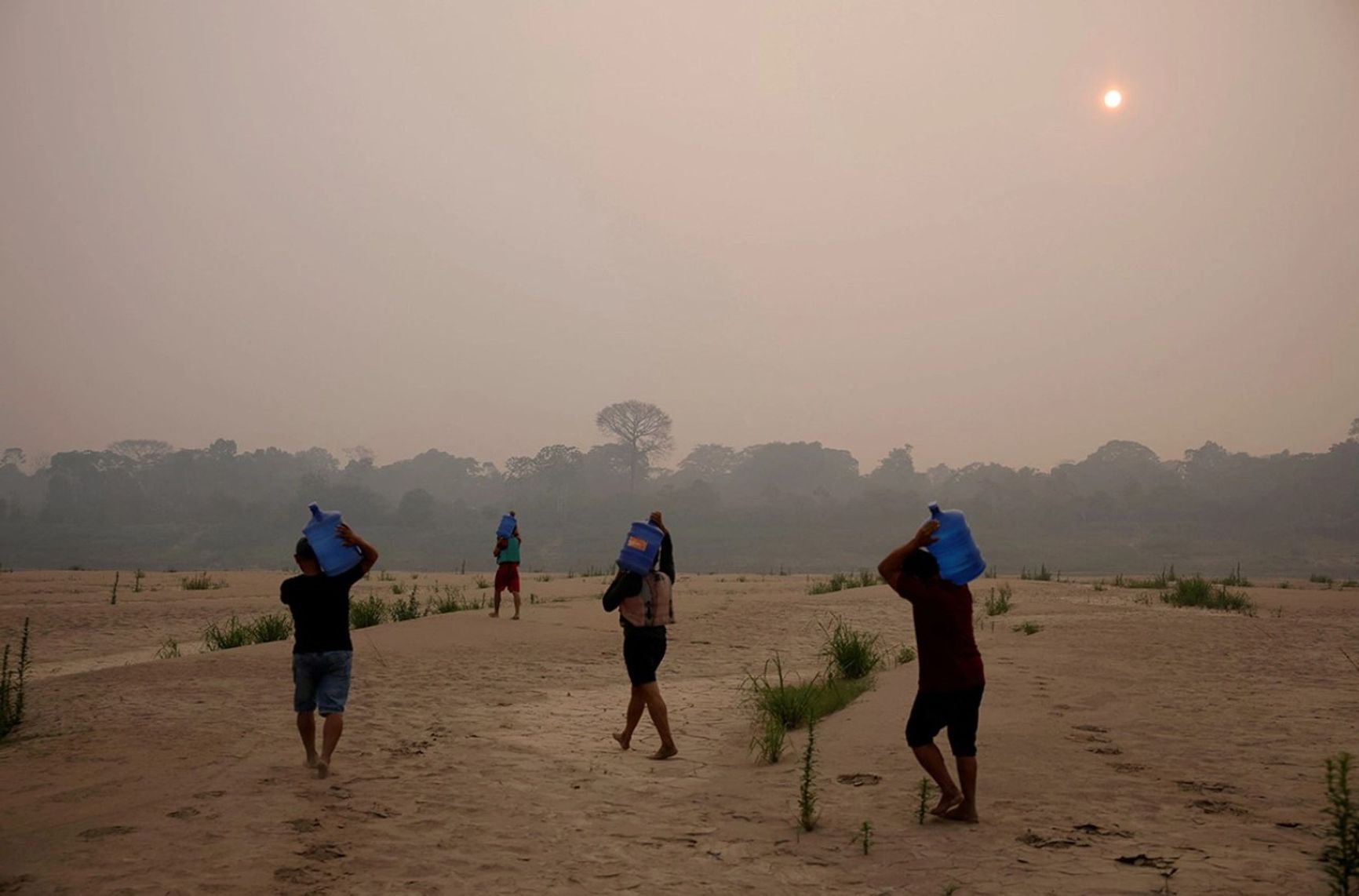 Locals carry water along the sandbanks of the Madeira River, Amazonas, Brazil. September 2024